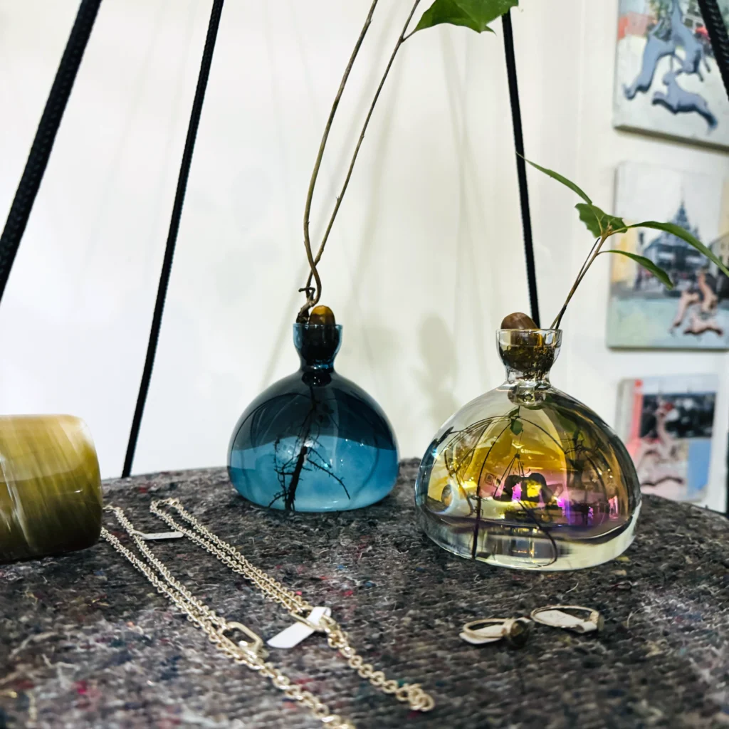 Zwei Eichelvasen in Blau und Perlmutt auf einem schwebenden Regal. Darauf befinden sich auch mehrere Schmuckstücke.